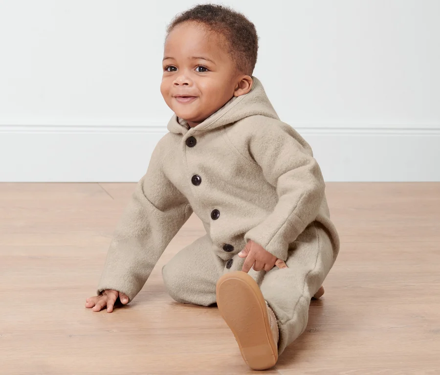 Kleinkind im Baby-Merino-Walkoverall sitzt auf dem Boden.