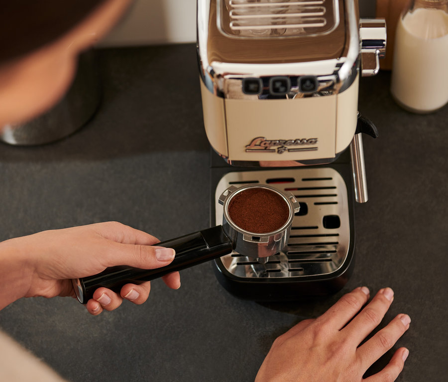 Frau hält »Lapressa« Siebträgermaschine in Creme mit gemahlenem Kaffee über Abtropfgitter.