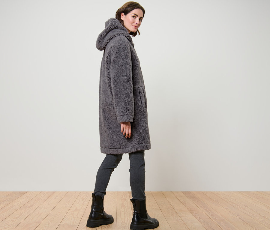 Frau posiert in einem grauen Teddymantel mit Kapuze.