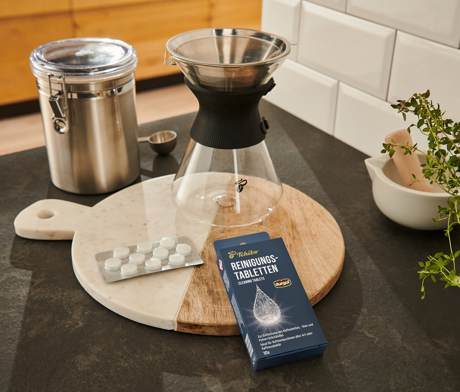 Auf einem Brett liegen durgol® Reinigungstabletten für Kaffeeöle, ein Behälter, ein Kaffeefilter und ein Messlöffel.