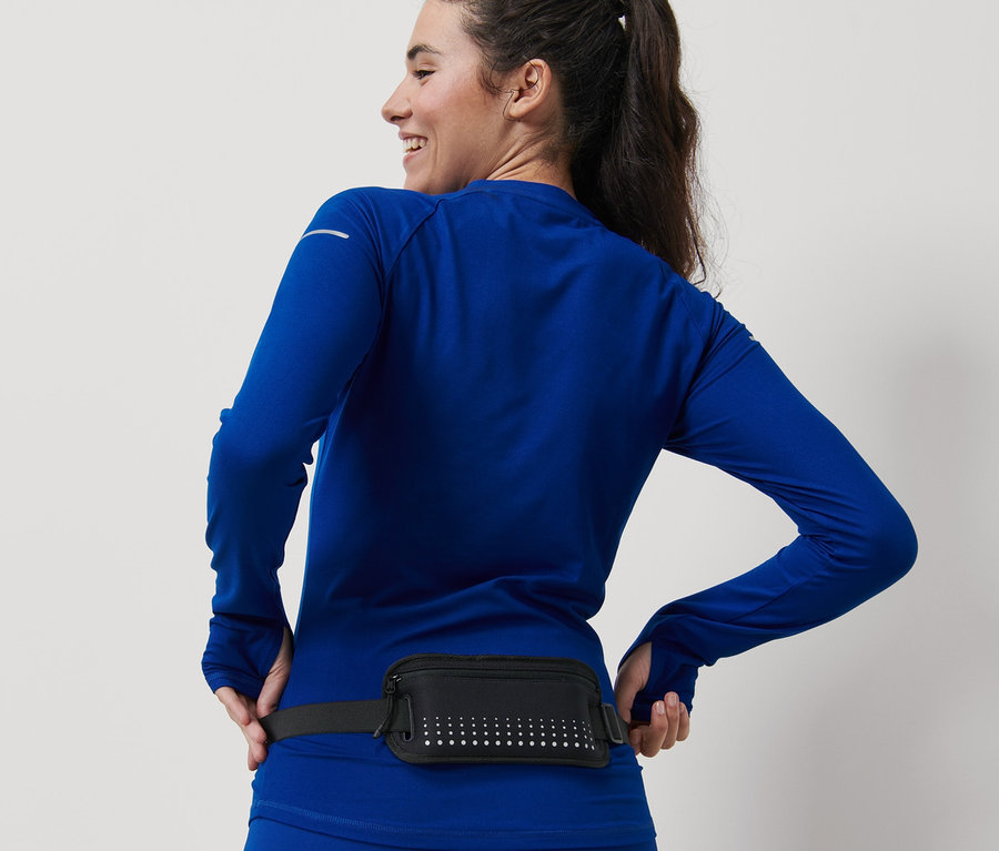 Lächelnde Frau in blauer Sportbekleidung trägt einen schwarzen Smartphone-Laufgürtel.