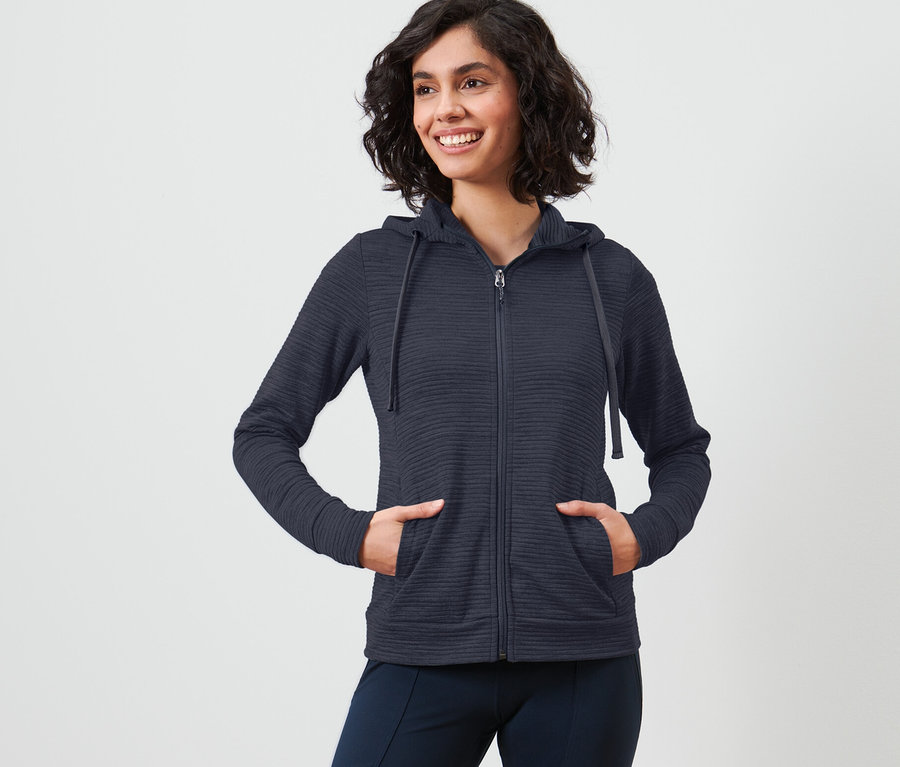 Frau mit kurzen Haaren posiert in blauer Kapuzenjacke.