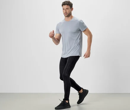 Mann in grauem T-Shirt und schwarzen Lauftights beim Laufen.