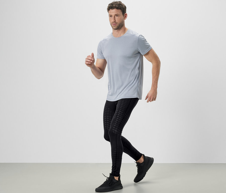 Mann in grauem T-Shirt und schwarzen Lauftights beim Laufen.