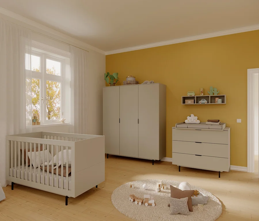 Ein Kinderzimmer mit einem Gitterbett, einer Kommode und einem Schrank. An der Wand befindet sich ein Regal und auf dem Boden ein Teppich mit Spielzeug. Zu sehen ist auch ein Stand-und-Wandregal »Tomino«.