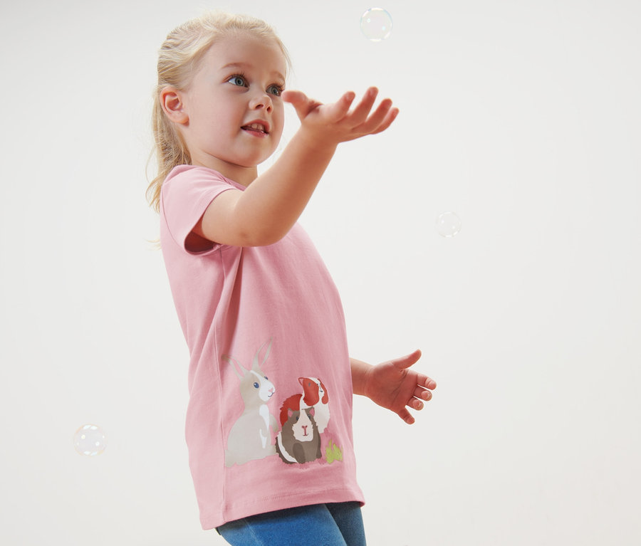 Mädchen fängt Seifenblasen. Sie trägt ein rosa T-Shirt mit Tiermotiven. 2 Kleinkind-T-Shirts.