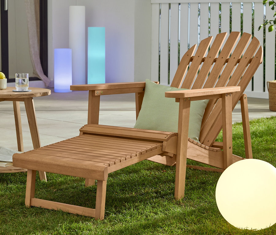 Auf Rasen stehen ein Adirondack Gartensessel mit ausziehbarem Fußteil in Naturfarbe, ein Beistelltisch »Lenja« mit 2 Ebenen in Teakoptik, eine Solar-Kugelleuchte (ca. 30 cm) und Solar-Lichtsäulen mit Farbwechsel.