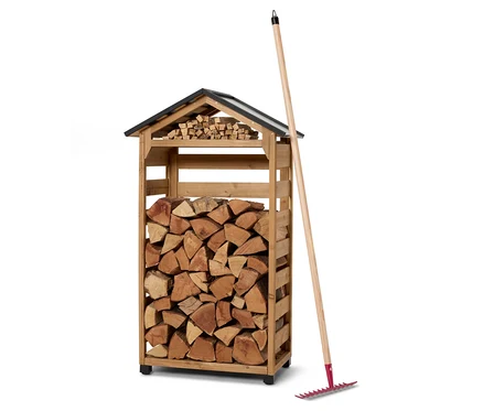 Ein Holzschuppen gefüllt mit Holz und ein Rechen, der daran lehnt.
