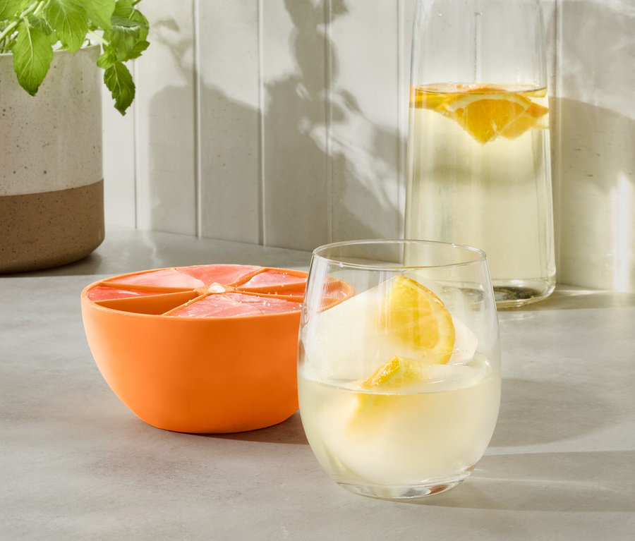 Oranger XL-Eiswürfelbereiter neben Glas mit Getränk und Wasserflasche.