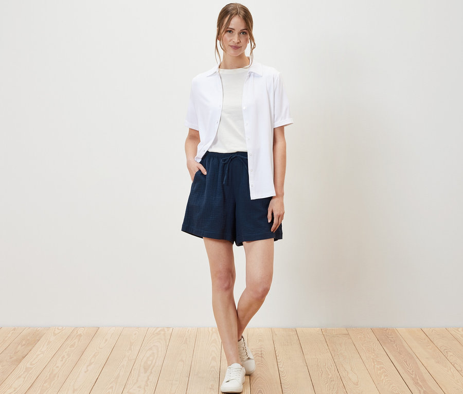 Eine Frau posiert in Musselin-Shorts, T-Shirt und Hemd.