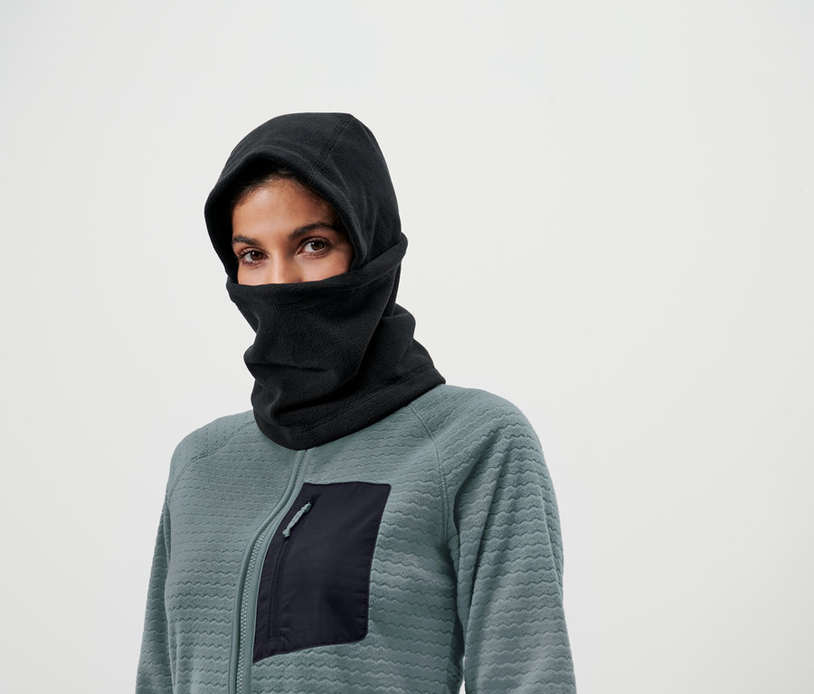 Frau mit braunen Augen trägt eine schwarze Sturmhaube und eine Sweatshirtjacke mit Reissverschluss und Tasche.