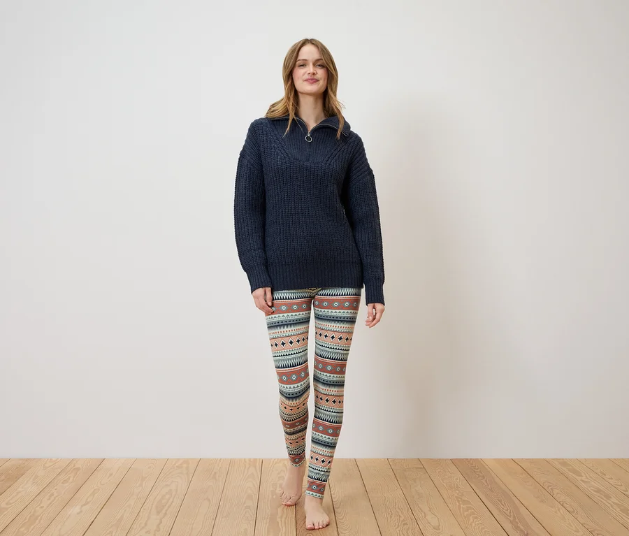 Eine Frau steht und trägt einen dunkelblauen Pullover und gemusterte Leggings.