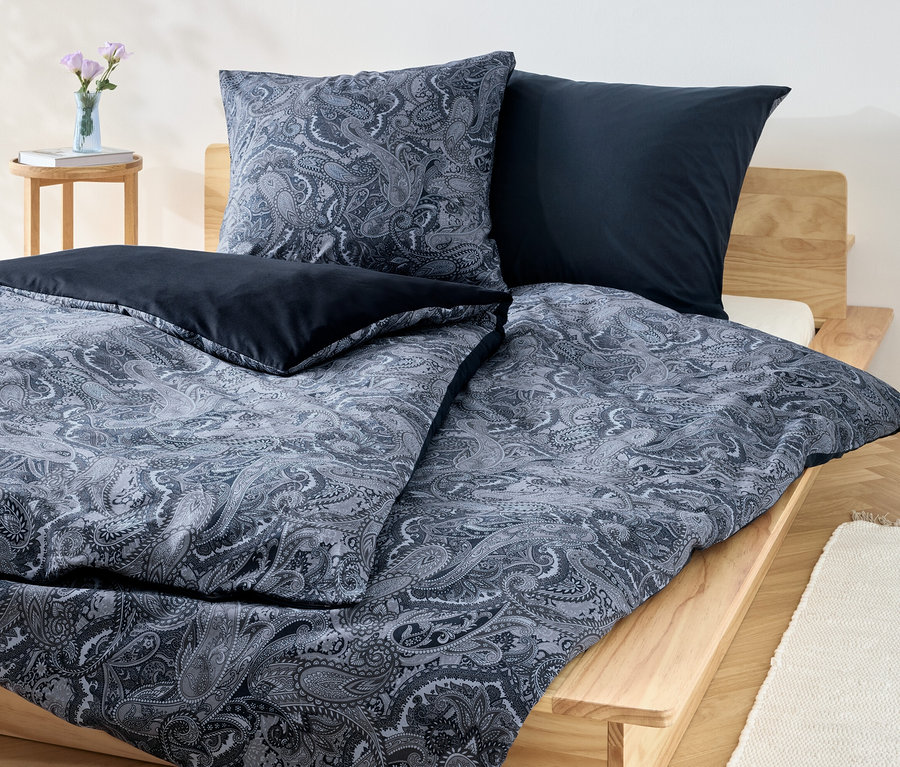 Ein blaues Renforcé-Bettwäsche-Set mit Blumenmuster und unifarbenen blauen Kissen auf einem Holzbett.