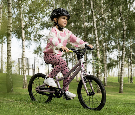 Ein Mädchen mit Helm fährt ein PUKY LS-PRO 18 Fahrrad in Pearl Pink auf einer Wiese.