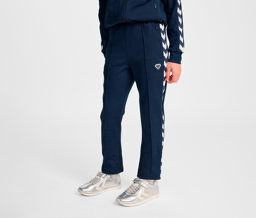 Person stehend, trägt marineblaue HUMMEL HMLJR Archive Regular Poly Pants und silberne Turnschuhe.