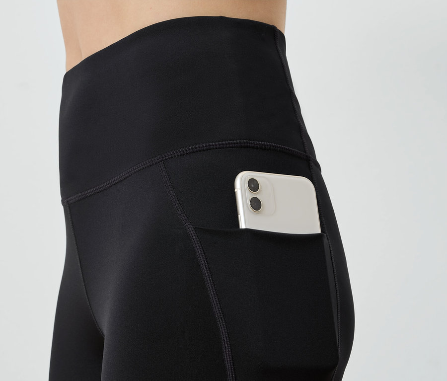 Schwarze Leggings mit einer Tasche, in der sich ein weißes Mobiltelefon befindet.