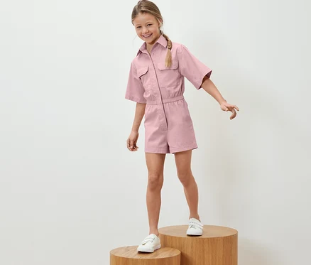 Mädchen steht auf Holzsockeln und trägt einen Kinder-Jumpsuit.