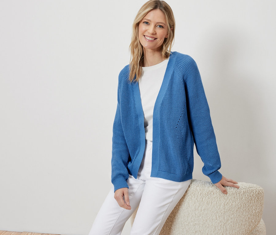 Frau sitzt und trägt einen offenen, blauen Cardigan.