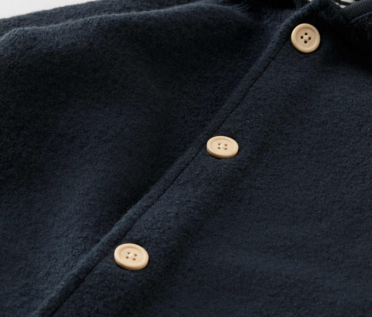 Detailansicht des marineblauen Baby-Walkoveralls mit Merinowolle und hellen Knöpfen.