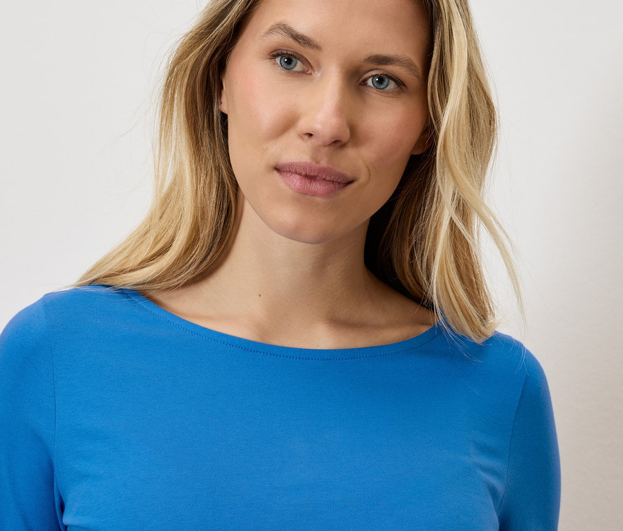 Porträt einer blonden Frau, die ein blaues Langarmshirt trägt.