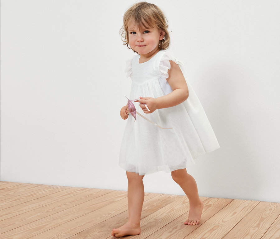 Kleines Mädchen in einem Baby-Tüllkleid geht über einen Holzboden.