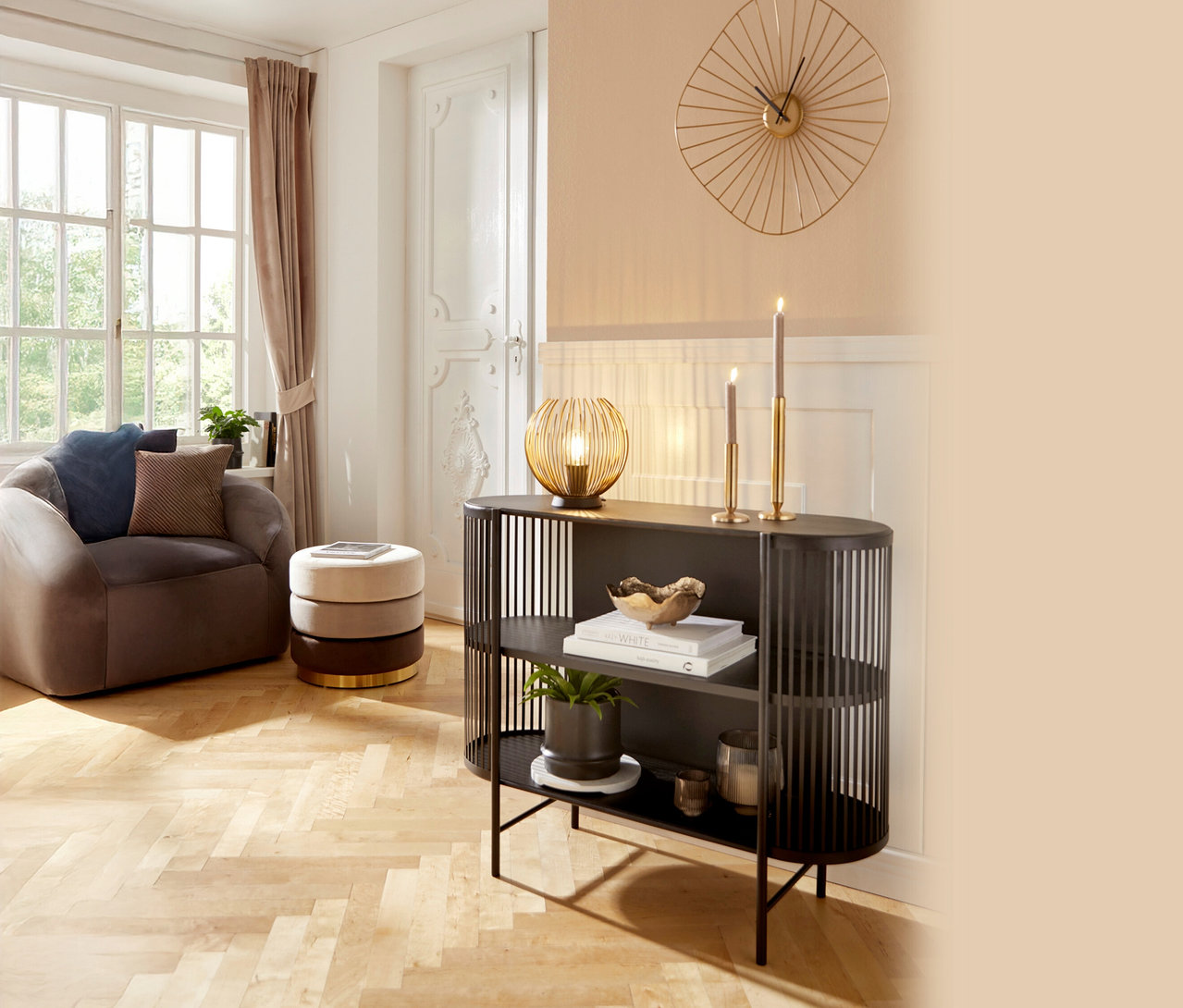Wohnzimmer mit braunem Sessel, gestapeltem Hocker und schwarzem Regal mit Dekorationen wie Lampe, Kerzen und Pflanze.
