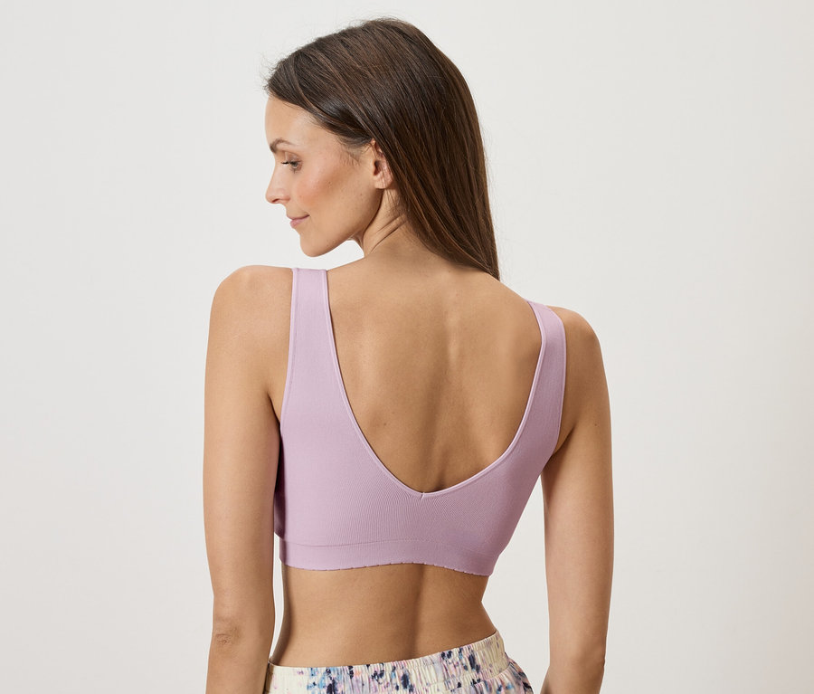 Rückansicht einer Frau mit braunen Haaren, die ein lila Sportoberteil und gemusterte Shorts trägt.