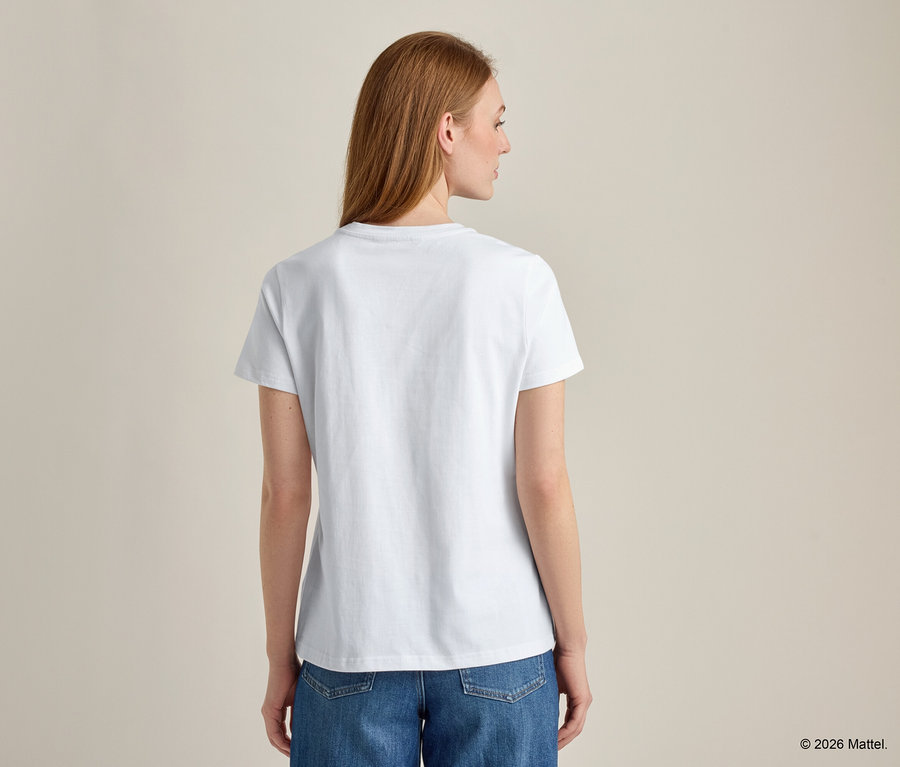 Rückansicht einer Frau mit langen roten Haaren, die ein weißes T-Shirt und blaue Jeans trägt.