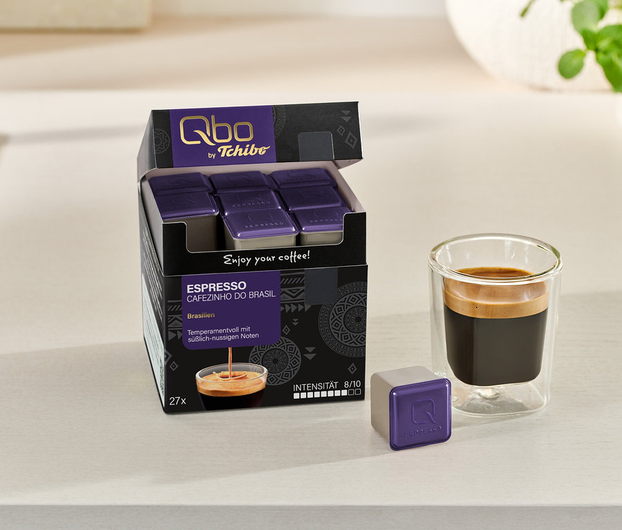 Geöffnete Packung Qbo Espresso CAFEZINHO DO BRASIL mit Kapseln und ein Espresso im Glas, daneben eine einzelne Kapsel.