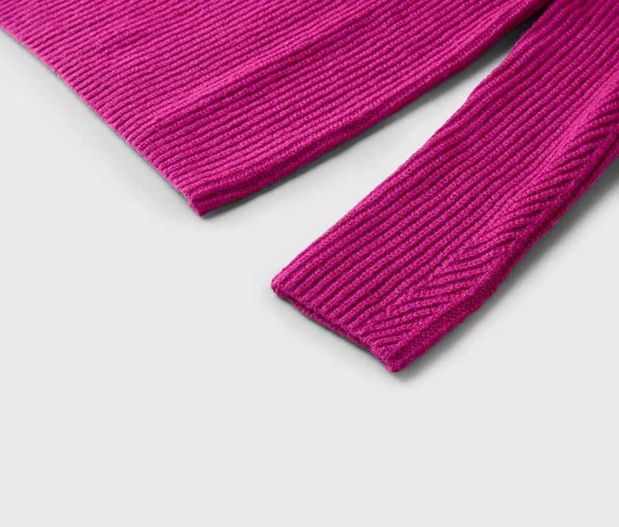 Nahaufnahme eines Ärmels und eines Teils des Rumpfes eines pinkfarbenen, gerippten Strickpullovers auf grauem Hintergrund.