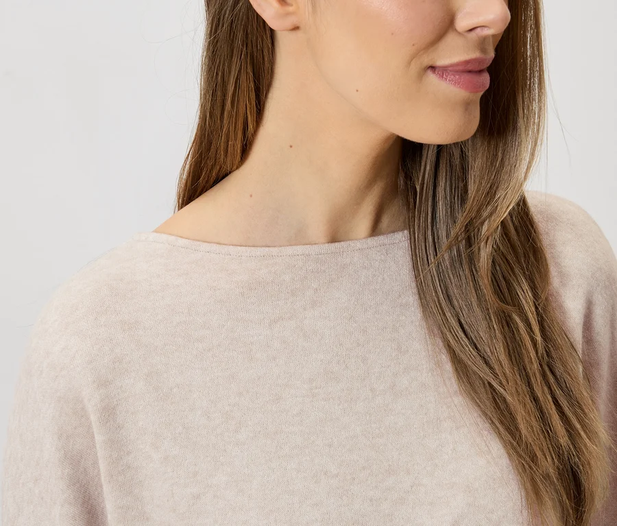 Nahaufnahme einer Frau mit langen braunen Haaren, die einen hellrosa Pullover mit Rundhalsausschnitt trägt.