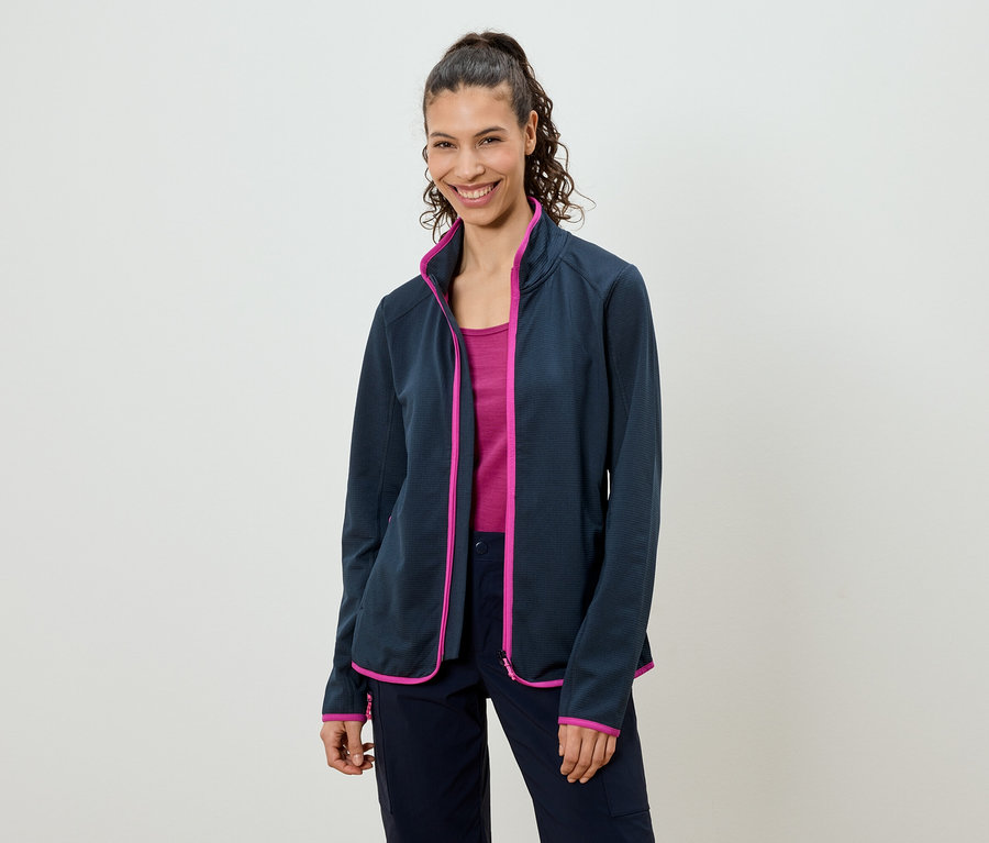 Frau mit Pferdeschwanz trägt eine marineblaue Fleecejacke mit pinkfarbenen Akzenten über einem pinkfarbenen Top und marineblauen Hosen.