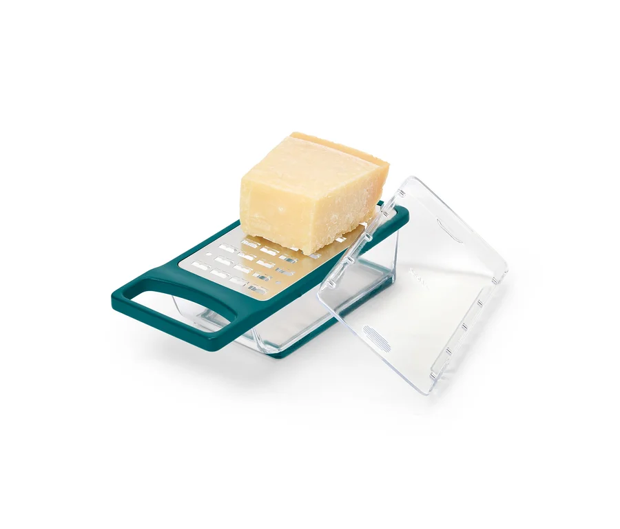 Ein Stück Käse liegt auf einer grünen Käsereibe mit Behälter.