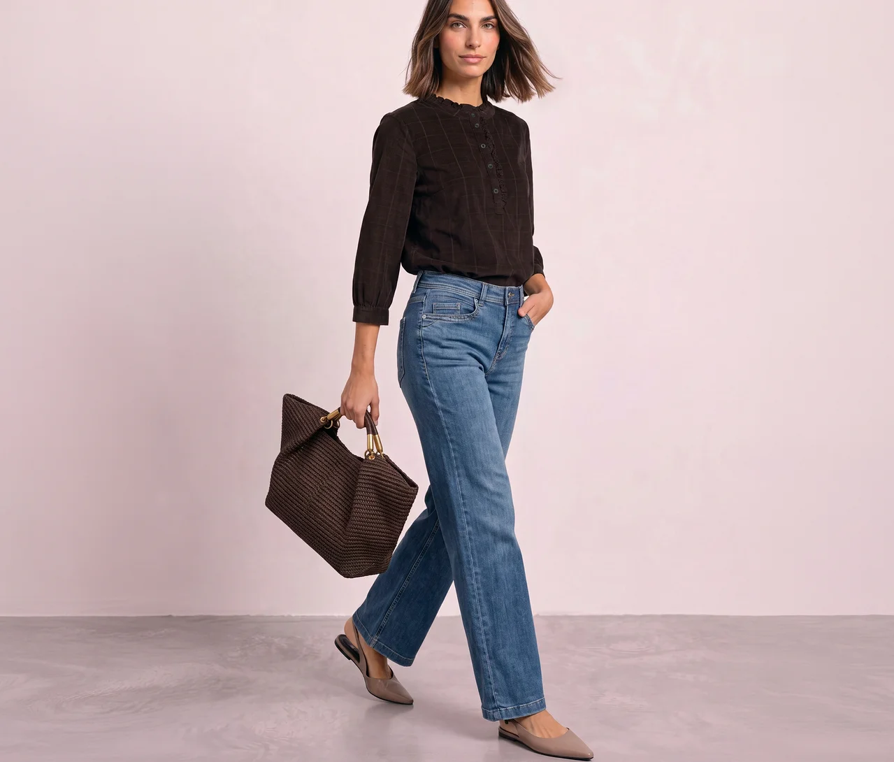 Eine Frau geht nach rechts, trägt eine braune Street One Cordbluse, blaue Jeans, hellgraue Schuhe und hält eine braune gewebte Tasche.