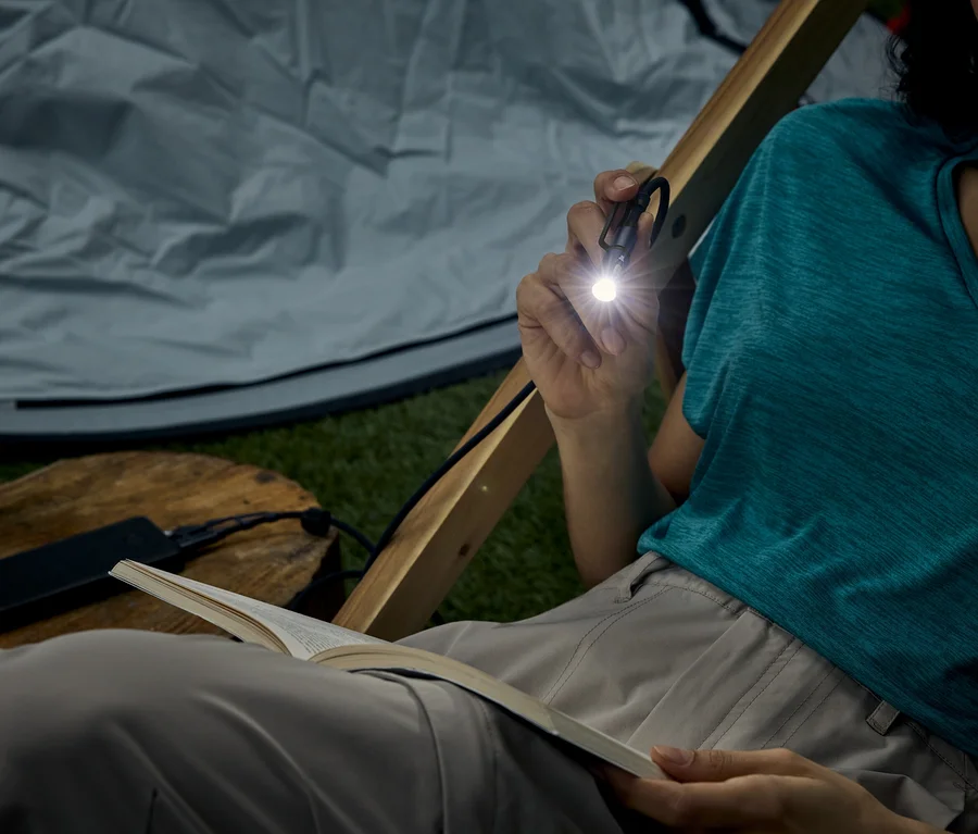 Frau sitzt im Zelt und liest ein Buch mit einer kleinen Taschenlampe, die sie hält.