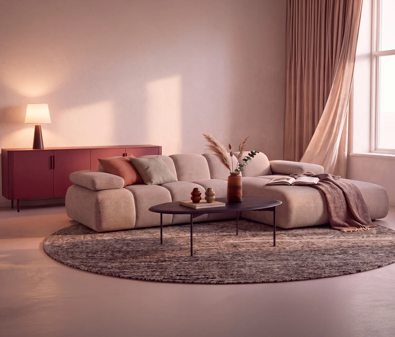 Ein gemütliches Wohnzimmer mit einem beigen WOOOD Sofa »Mojo« mit Recamiere rechts, einem dunklen ovalen Couchtisch und einem runden Woood Teppich »Efia« (Ø 200 cm). Ein rotes Sideboard mit einer Lampe steht an der Wand, und rosafarbene Vorhänge rahmen ein Fenster ein.