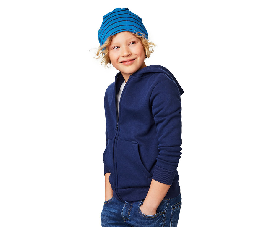 Blonder Junge trägt eine blaue Wendemütze und eine blaue Reißverschlussjacke.