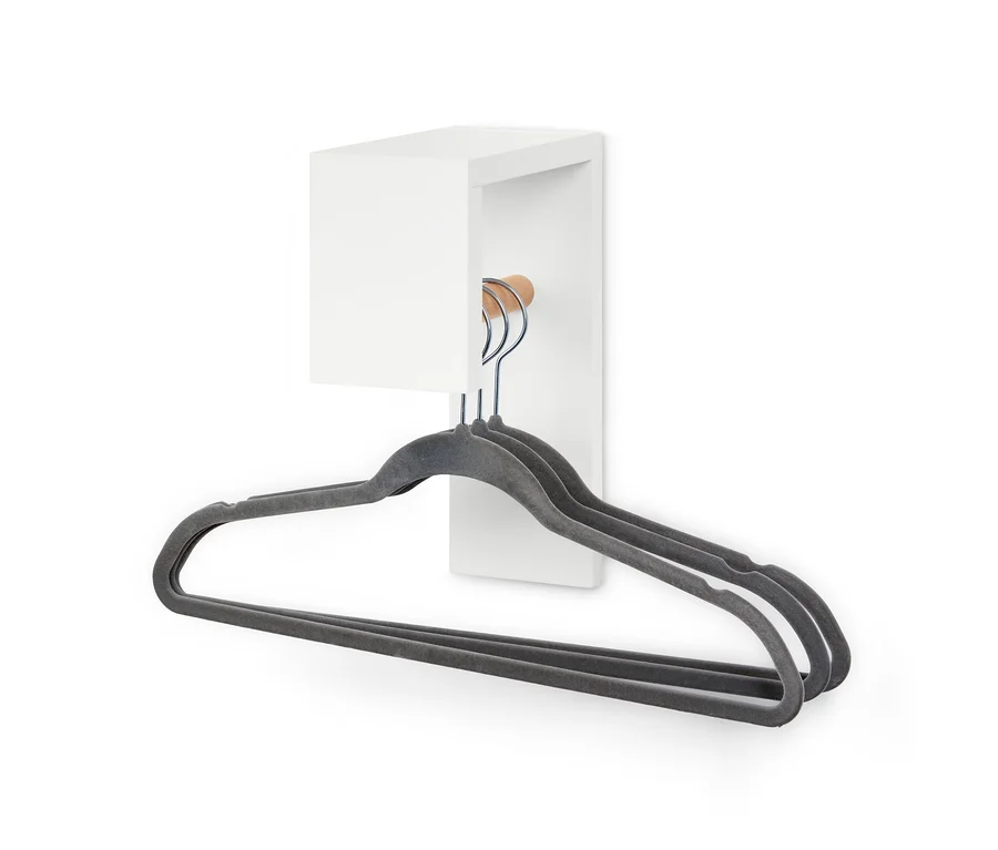 Drei graue Kleiderbügel hängen an einer kleinen Garderobe.