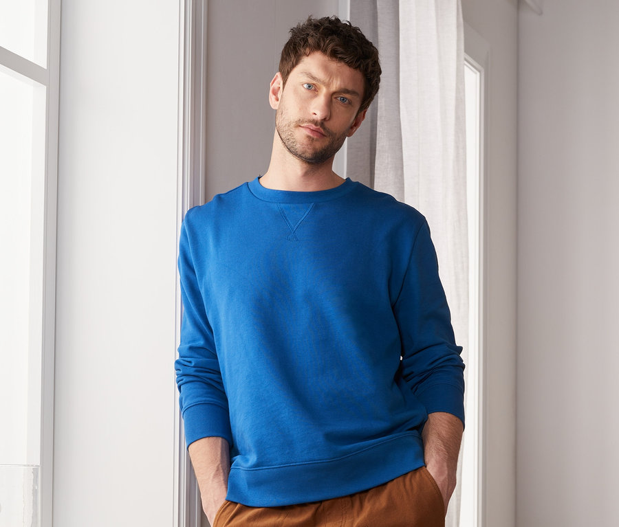 Mann posiert in blauem Sweatshirt.