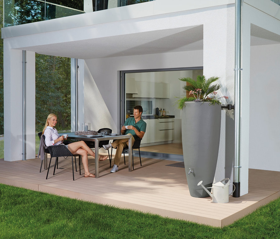 Zwei Personen sitzen draußen an einem Tisch neben einem grauen Garantia 2-in-1-Regentonne-Komplett-Set, ca. 300 l.