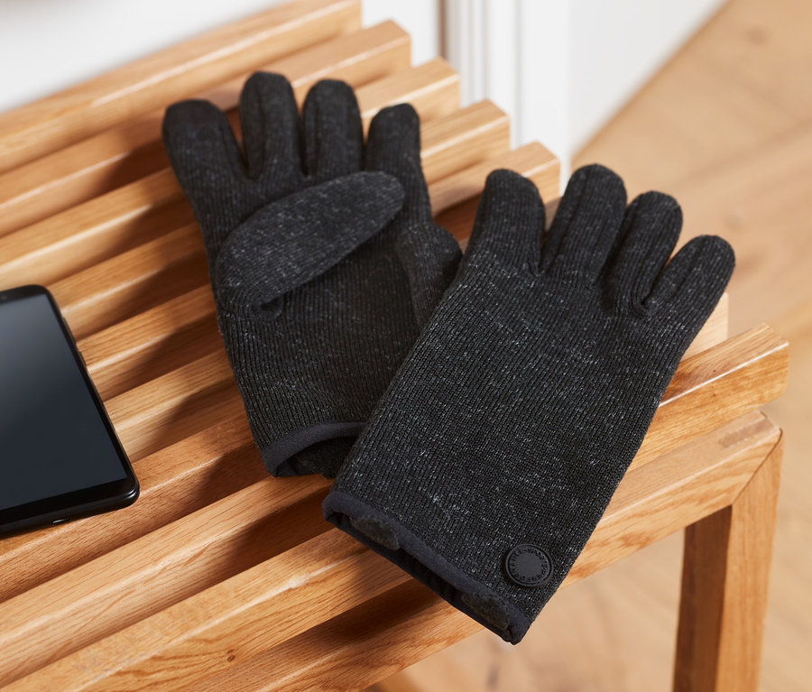 Zwei Strickfleece-Handschuhe liegen auf einer Holzbank neben einem Handy.