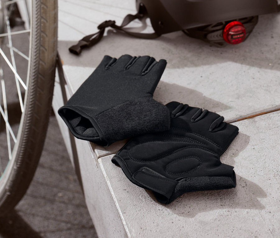 Schwarze Fahrrad-Handschuhe liegen neben einem Fahrrad und einem Helm.