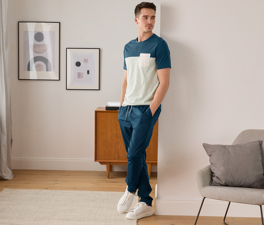 Mann lehnt in blauem T-Shirt und Comfort-Chino an der Wand.