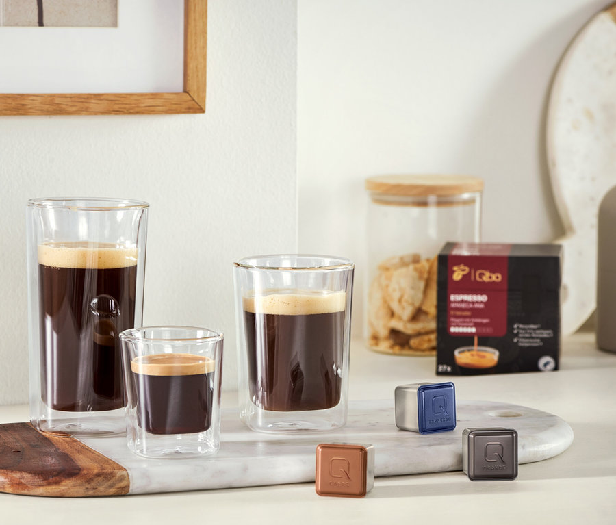 Drei unterschiedlich große Gläser mit Kaffee stehen auf einem Marmortablett neben einer Packung Kapseln und drei Kaffeekapseln. Zu sehen sind 2 Caffè Crema Gläser und 2 Espresso Gläser.