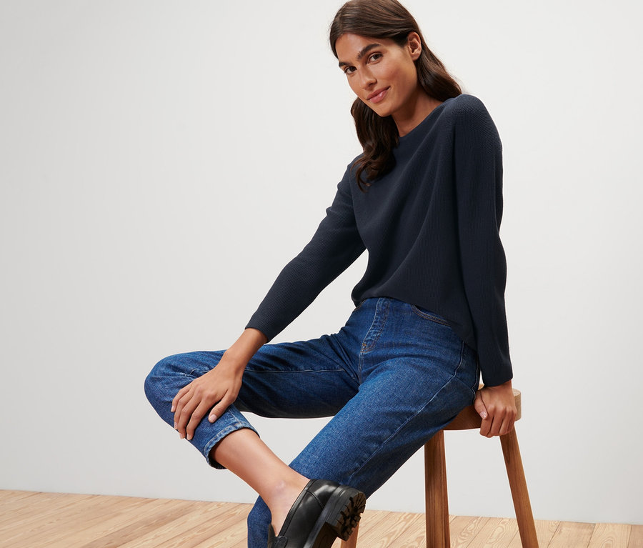 Frau sitzt auf Hocker und trägt dunkelblauen Strickpullover.