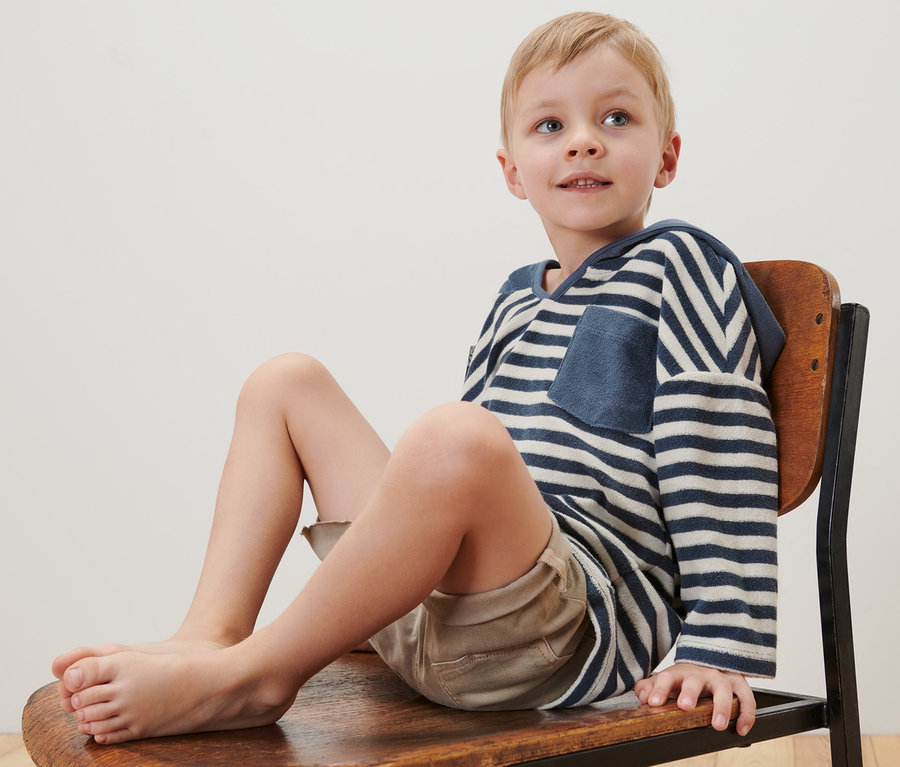 Junge sitzt auf Stuhl, trägt Kinder-Frottier-Shirt.
