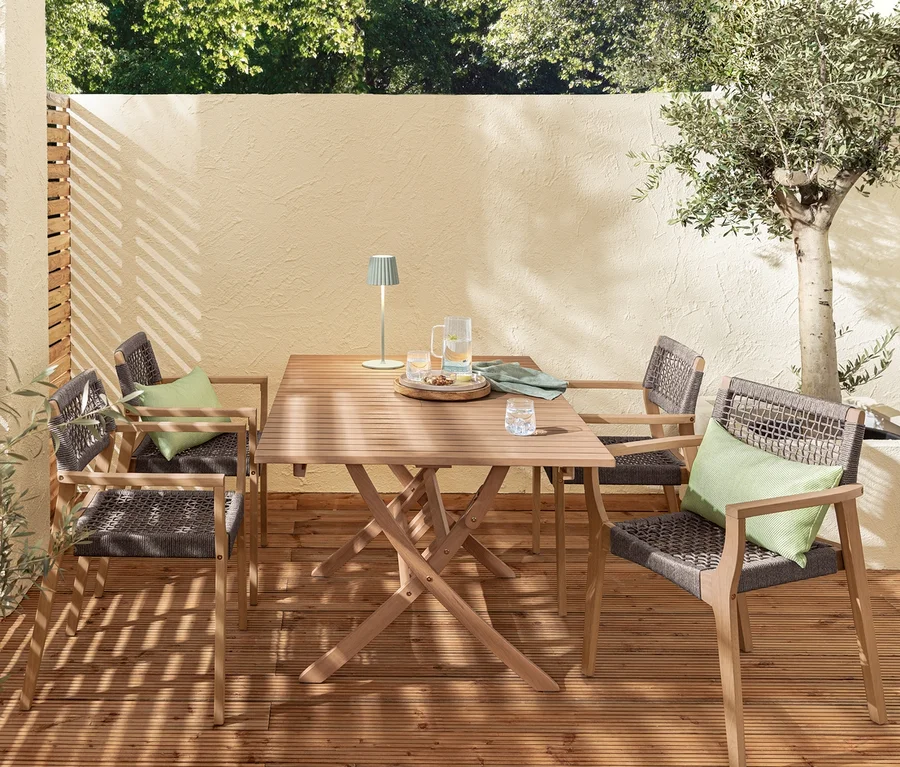 Ein Gartensitzplatz mit einem ausziehbaren Klapptisch »Lenja«, zwei salbeifarbene LED-Akku-Tischleuchten, stapelbaren Dining-Stühlen und einer dekorativen Coolbox mit Flaschenöffner.