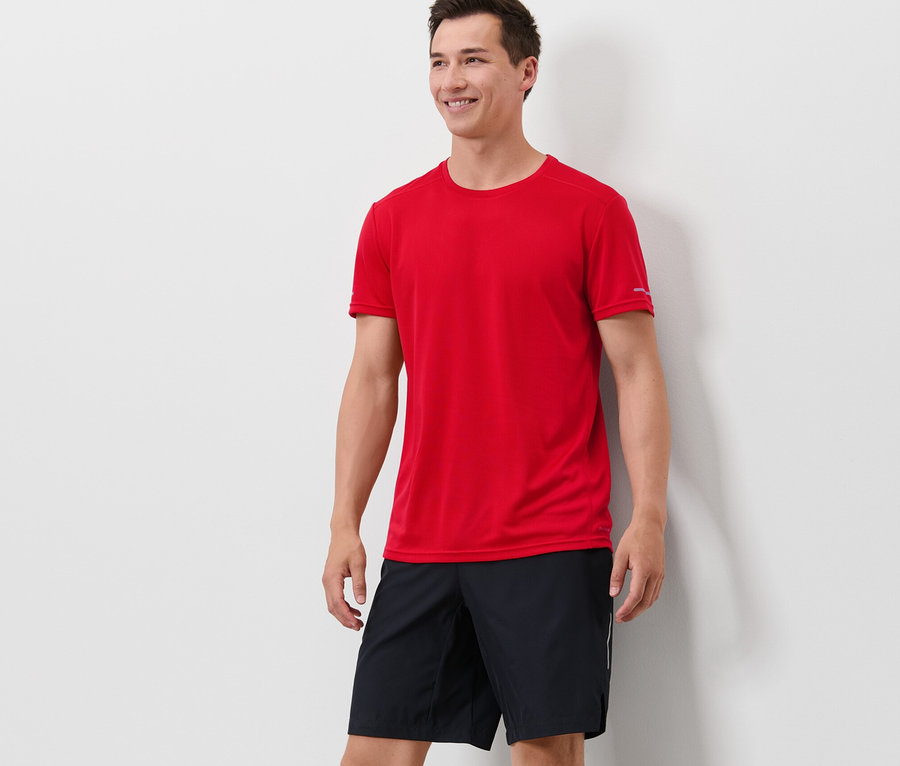 Mann steht und trägt ein rotes Funktionsshirt und schwarze Shorts.
