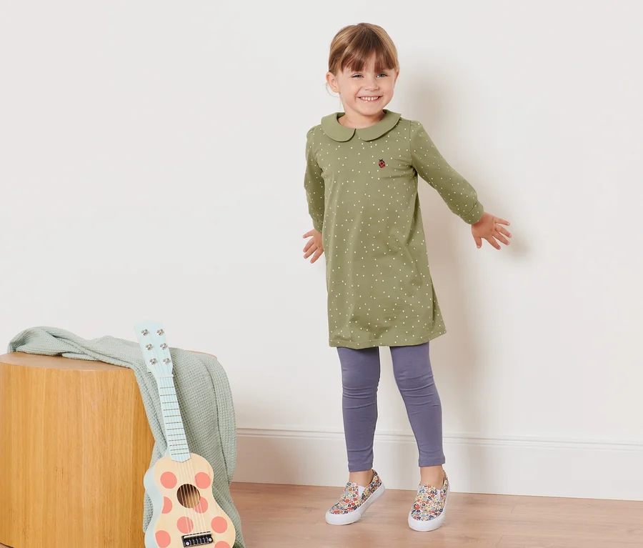 Lächelndes Mädchen posiert in einem olivgrünen Kleinkinder-Jerseykleid mit Kragen und Tupfen.