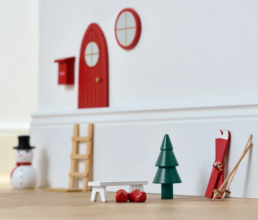 Weihnachtliche Miniaturdekoration: rote Tür, Fenster, Baum, Ski und Schneemann.